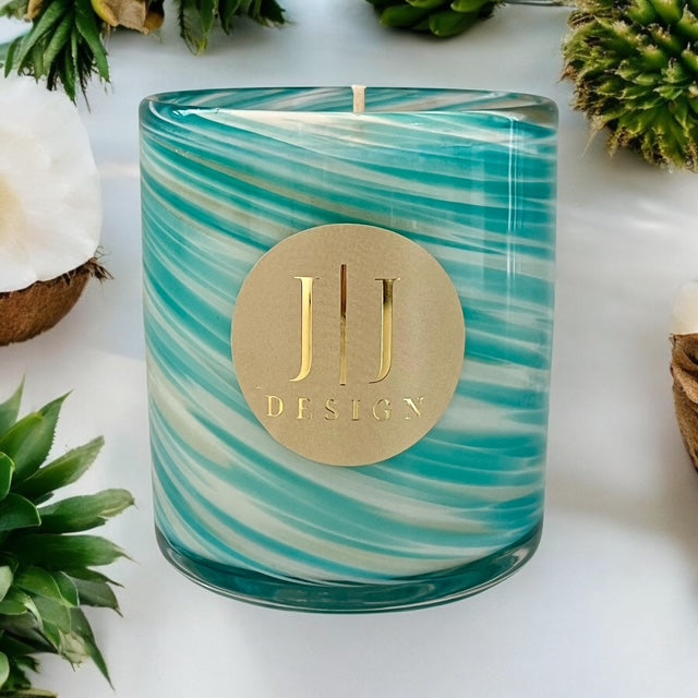 Coconut Guava scented soy candle 400g by JJ Design – hand poured, turquoise wax, and a gold label that reads 'JJ Design' on a white surface, surrounded by green foliage and a brown tumbler.