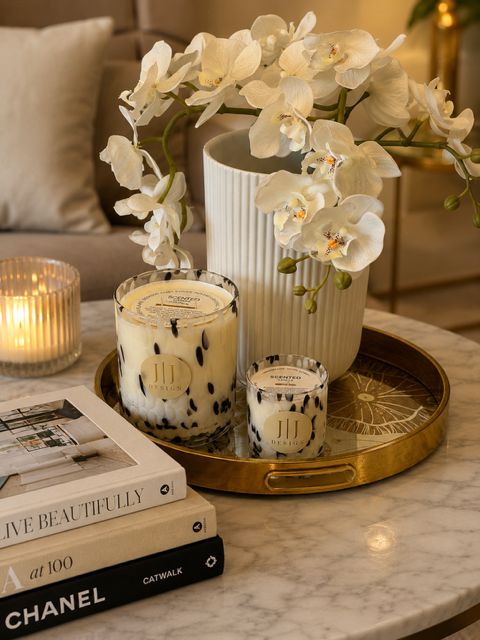 Candles on a gold tray on a marble coffee table with a stack of three books..