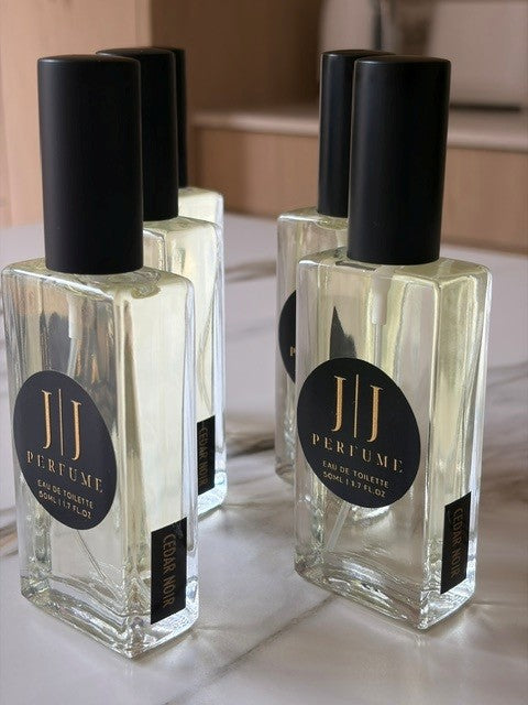Four JJ Perfume bottles with black caps on a marble surface.